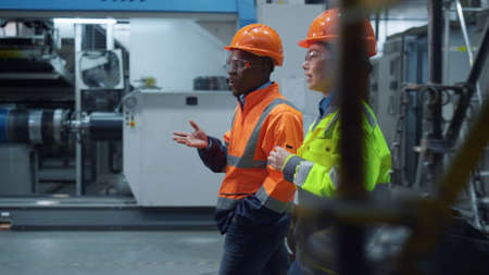 Attractive specialists colleagues walking wearing special uniform at factory. Woman industrial...