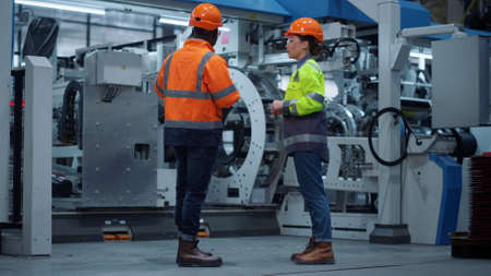 Professional supervisors discussing project at modern machinery factory. Multiethnic couple engineer...