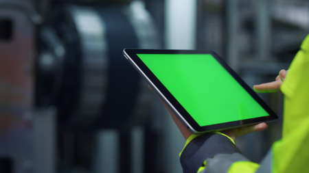 Hands scrolling greenscreen tablet computer on modern production factory. Closeup unrecognizable...