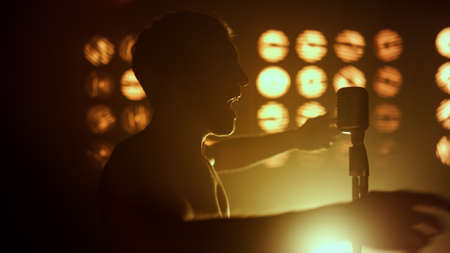Silhouette unknown performer singing emotional on stage show close up. Professional vocalist performing firely in nightclub lights. Unrecognizable young man dancing near microphone with excitement.の写真素材