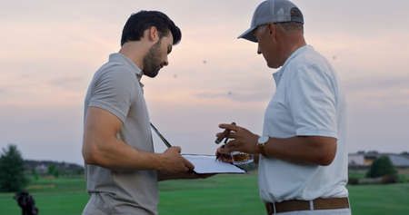 Golf men sign document contract on golfing course. Two businessmen make deal at countryside club...