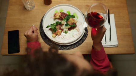 Woman eating restaurant meal drinking wine glass at luxury cafe table. Unknown african american lady enjoying evening alone in fancy bar close up. Businesswoman dining on dinner date. Tasty concept.の写真素材