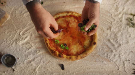 Chef hands preparing traditional italian pizza recipe at restaurant. Close up pastry cook adding...