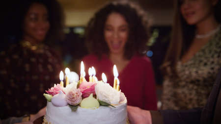 Friends surprising birthday girl at celebration party. Close up burning candles in cake. Happy...
