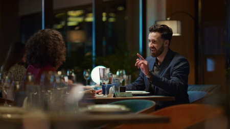Multiethnic couple enjoying romantic dinner date in elegant night restaurant. Mixed race lovers flirting spending time together in luxury hotel cafe. Two people talking at evening. Romance concept.の写真素材
