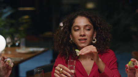 African american girl drinking shot on friends meeting at fancy restaurant bar. Close up afro hair woman enjoying alcohol in group party celebration. Young people hang out in cafe. Having fun concept.の写真素材