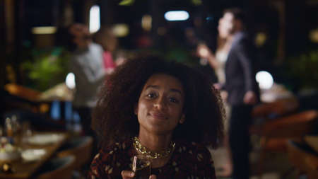 African american girl dancing on friends meeting party. Fancy woman holding champagne drink glass in restaurant. Young lady celebrating birthday with people group in bar. Having fun leisure concept.の写真素材