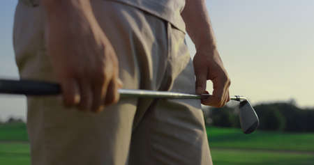 Golfer hands holding club putter on sunset course field. Man enjoy golf outdoors close up. Unknown...