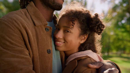Portrait african american daughter looking camera. Unknown dad hold kid in arms. Joyful relaxed girl enjoying time with father sunny park. Happy curly-haired kid resting together with loving parent.の写真素材