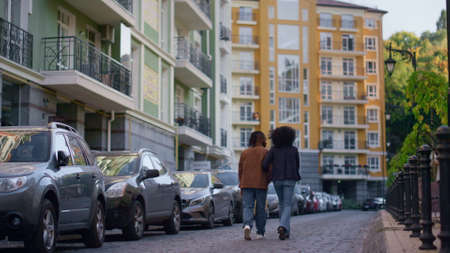 Married couple walking together at modern city residential complex rear view. Lovely african american woman man enjoying warm evening going town street. Relaxed lovers talking enjoying time on date.の写真素材