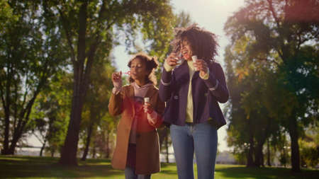 Joyful family blowing soap bubbles standing in green park. Happy leisure time. Attractive african...