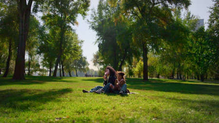 Joyful child mom blowing soap bubbles in sunny park. Family picnic on spring day. Beautiful african...