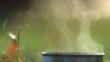 Light vapor hot tea rising over  mug close up. Tranquil scenery metal cup with warm drink standing...
