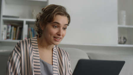 Surprised woman talking video conference with friend in pajamas home closeup. Beautiful girl student...