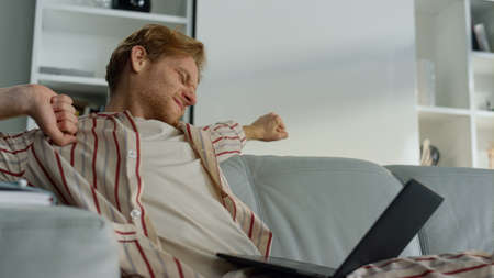 Tired guy browsing web at home office closeup. Sleepy manager stretching body working computer...