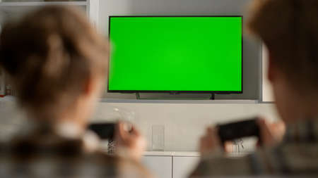 Friends playing green tv screen video game at home. Chroma key flat screen set. Unrecognized gamers...