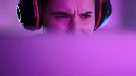Beautiful neon gamer playing computer game in pink neon lights at home closeup. Attractive focused...