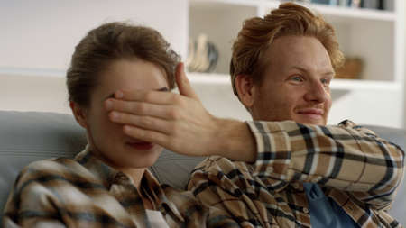 Married people watching tv program at home closeup. Ginger man close woman eyes. Beautiful family resting together in living room. Playful redhead husband joking have fun of frustrated bored wife.の写真素材