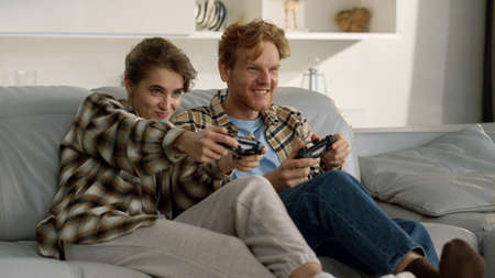 Competitive wife playing video game with smiling ginger husband in living room. Focused happy family...