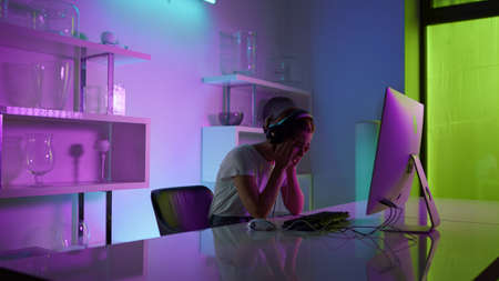 Competitive gamer playing esport computer game at neon lights home closeup. Emotional beautiful girl losing virtual battle in headset on weekend night. Upset woman looking screen check round results.の写真素材