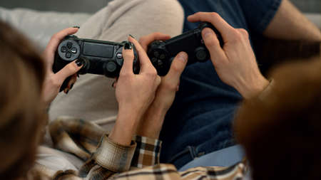 Couple hands using joysticks at home closeup. People having fun play video game. Unrecognized man...