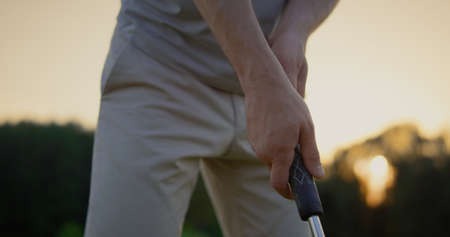 Professional golf player hands holding club putter on sunset fairway field. Close up golfer getting ready hitting ball on golfing course game. Unrecognizable sportsman prepare playing. Hobby concept.の写真素材