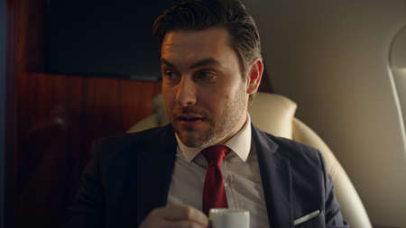Closeup luxury businessman traveling on private jet. Happy man drinking coffee talking with unknown...