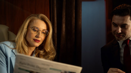 Closeup business couple discussing newspaper on airplane trip in golden sunlight. Attractive blonde...