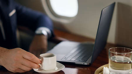 Relaxed businessman working computer on trip. Closeup hand putting coffee cup tapping laptop at...