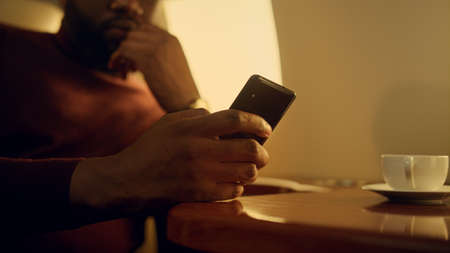 Focused businessman checking smartphone email. Hands holding cell phone closeup. Pensive african...