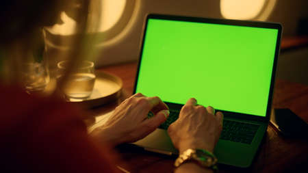 Hands typing green laptop closeup. Airplane passenger resting browsing internet. Unrecognized...