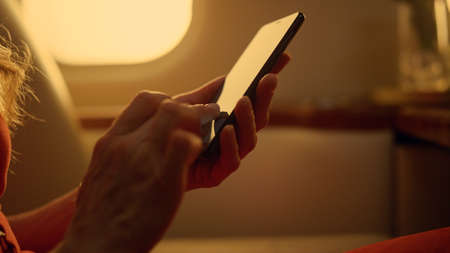 Plane passenger holding smartphone in hands closeup. Manager working on trip checking email. Unknown luxury woman rest browsing web making online order in first class jet. Business travel concept.の写真素材