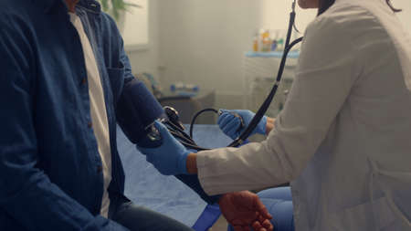 Therapist checking blood pressure senior patient in modern clinic close up. Woman doctor examining old man pulse using stethoscope. Cardiologist checkup hypertonic pensioner with medical tonometer.の写真素材