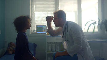 Physician testing pupil reflex shining flashlight in teen girl eyes. European doctor checking...