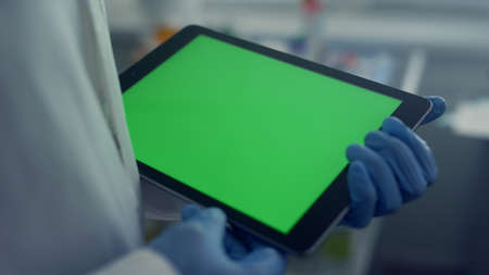 Doctor hands working on digital tablet computer close up. Unknown physician wearing gloves scrolling touchscreen modern pad in healthcare clinic. Medic touching green screen gadget in hospital.の写真素材
