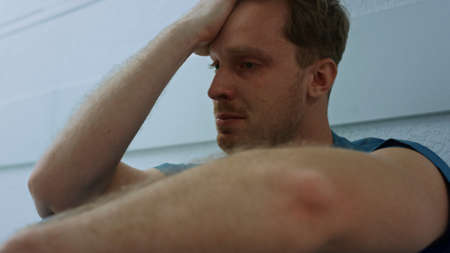 Upset overworked doctor holding hand on face sitting floor hospital corridor closeup. Tired young...
