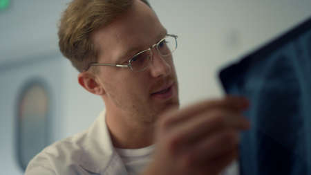 Focused therapist examining x-ray patient lungs in modern clinic close up. Man doctor diagnosing online using computer in coronavirus pandemic. Medical specialist working remotely in hospital office.の写真素材