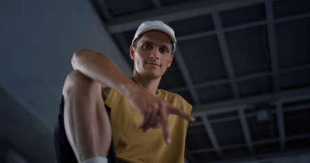 Attractive teenager resting at skate park. Casual active man looking on camera at urban space....