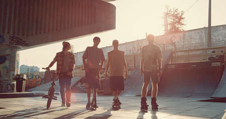 Teens friends skateboarder bmx rider roller skater and scooter rider walking together at urban skate...