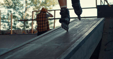 Extreme roller skater riding in ramp at urban space. Closeup male legs in roller blades skating fast outdoors. Close up unknown teens enjoying extreme sport at city skate park. Leisure concept.の写真素材