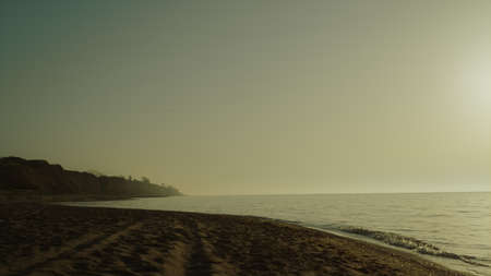 Beautiful view sandy beach at sunrise summer time. Scenic morning on nature near calm ocean. Clear sky under empty seacoast. Picturesque landscape of sea waves washing wide seashore at sunset.の写真素材