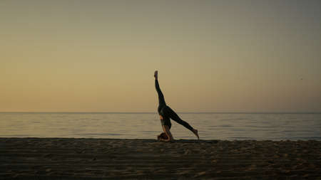 Silhouette sporty woman training twine standing on head outdoors. Flexible girl practicing yoga...