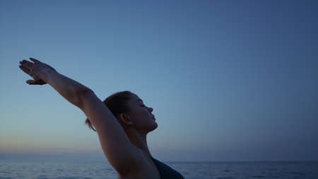 Fit girl performing virabhadrasana on beach close up. Strong woman standing warrior pose in front...