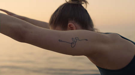 Athletic hot woman body standing warrior asana on seacoast closeup. Slim sportswoman practicing...