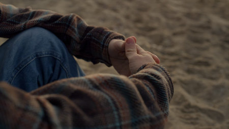 Unrecognizable man sitting on sandy beach alone. Closeup guy clasped hands in lock. Nervous male person moving fingers. Unknown man gesturing hands. Hipster wearing casual clothes. Stress conceptの写真素材