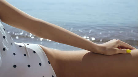 Sexy attractive girl posing on beach wearing white polka dot swimsuit closeup. View of seductive...