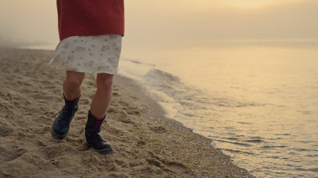 Fashionable girl in boots jumping on beach. Closeup young woman feet turning around. Female hipster legs dancing at ocean coast. Playful lady enjoying outdoor activity. Sunrise scene at sea shoreの写真素材