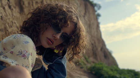 Portrait of seductive girl wearing stylish sunglasses in front sand hill. Attractive curly lady...