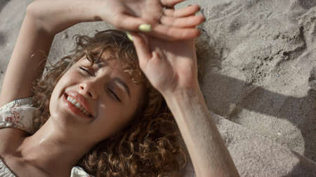 Seductive happy lady lying beach sand hiding face behind hands close up. Relaxed attractive woman smiling camera relaxing on sunny seashore. Cheerful carefree girl have fun on summer weekend.の写真素材