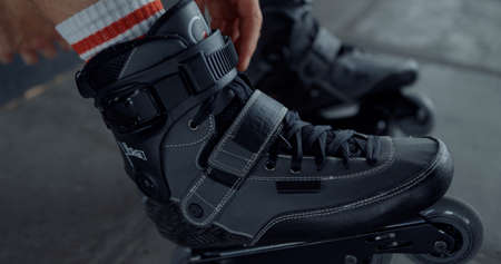 Active teenager putting on roller skates at skate park. Closeup unknown skater preparing for...